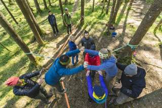 Gruppe an Jugendlichen balanciert auf zwischen Bäumen gespannten Slacklines